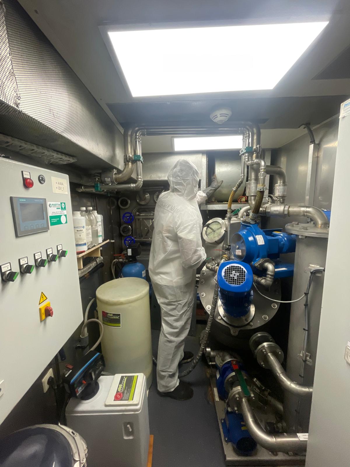 Monteur in beschermend pak inspecteert ventilatie-installatie